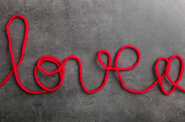 Word LOVE made of red thread on grey background