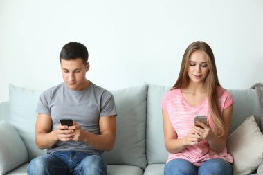 Cep telefonlarıyla evde koltukta oturan genç çift