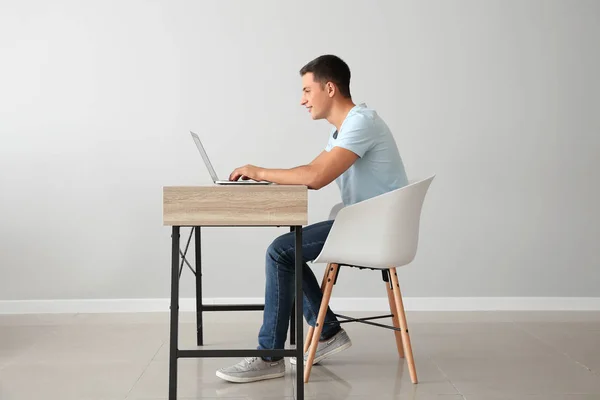 Νεαρός Εργασίας Φορητό Υπολογιστή Ενώ Κάθεται Στο Τραπέζι Φως Τοίχο — Φωτογραφία Αρχείου