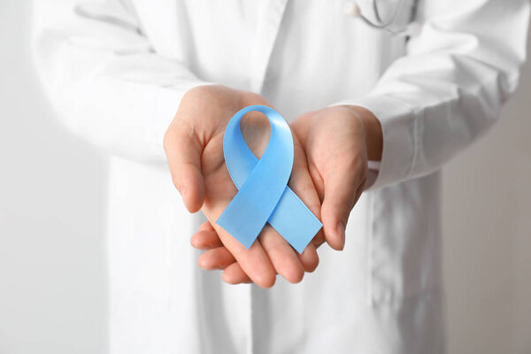 Female doctor holding blue ribbon, closeup. Cancer awareness concept