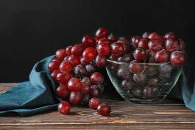Glass bowl with red grapes on wooden table clipart