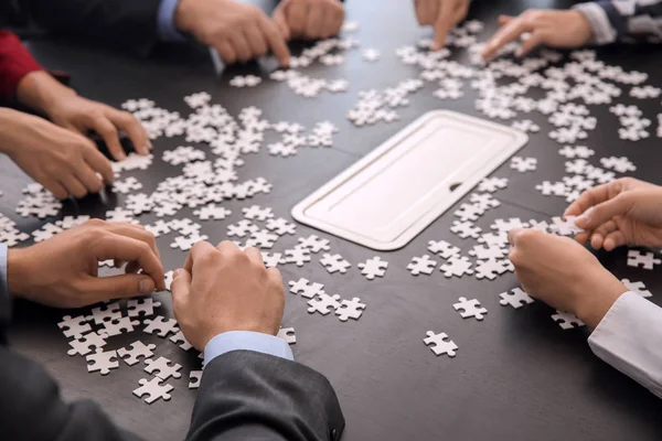 Business team assembling puzzle on dark table