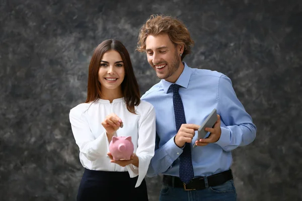 成功的年轻夫妇与小猪银行和计算器灰色背景 — 图库照片