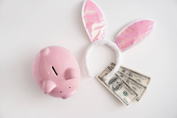 Piggy bank, bunny ears and dollars on white background. Concept of saving money for holiday
