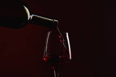 Bir şişe kırmızı şarap cam içine koyu arka plan üzerine dökülen