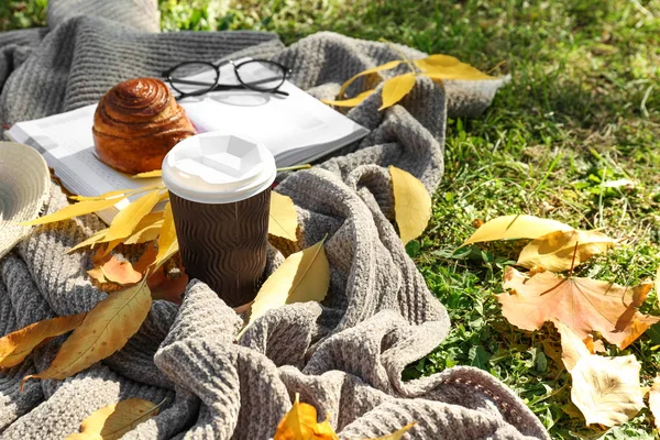 Cup of hot coffee with bun, notebook and autumn leaves on warm plaid