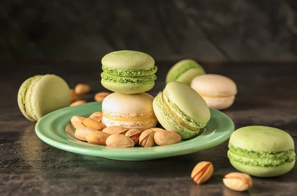 Plate with sweet macaroons and pistachio nuts on dark background