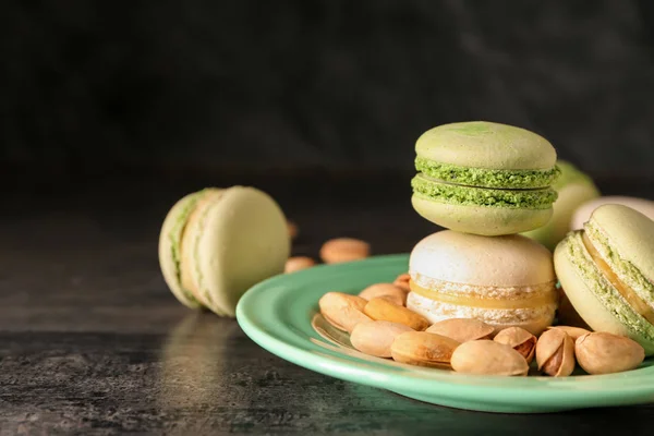 Plate with sweet macaroons and pistachio nuts on dark background, closeup