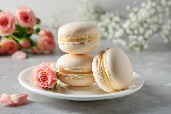 Plate with sweet macaroons and rose on grey table