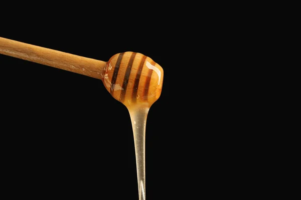 暗い背景に木製ディッパーから注ぐ蜂蜜 — ストック写真