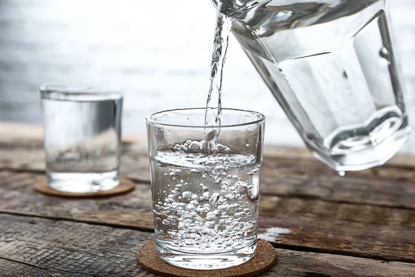 木製テーブルの上のガラスの水差しからの新鮮な水の注ぐ — ストック写真