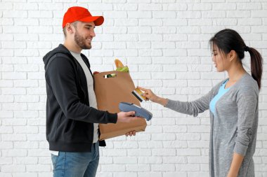 Asyalı kadın tuğla duvar arka plan üzerinde kredi kartı ödeme banka terminal kullanarak. Gıda dağıtım hizmeti