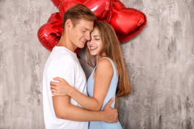 Gri duvarının yakınında kırmızı balon şeklinde kalbi olan genç çift