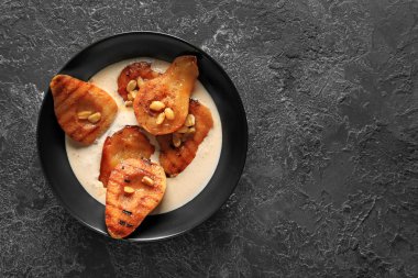 Izgara armut, krema ve karanlık tabloda fıstık ile kase