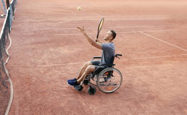 Young man in wheelchair playing tennis on court clipart