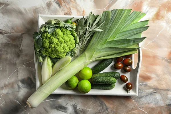 Tray with various fresh vegetables on color table