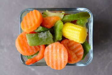 Gri arka plan üzerinde dondurulmuş sebzeler ile cam kase