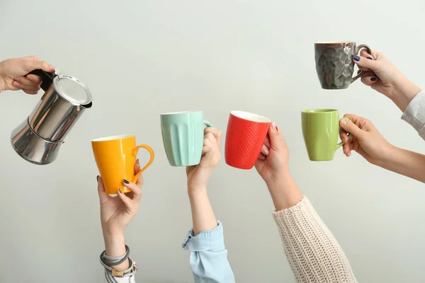 Woman pouring coffee into cups in hands of people on light background