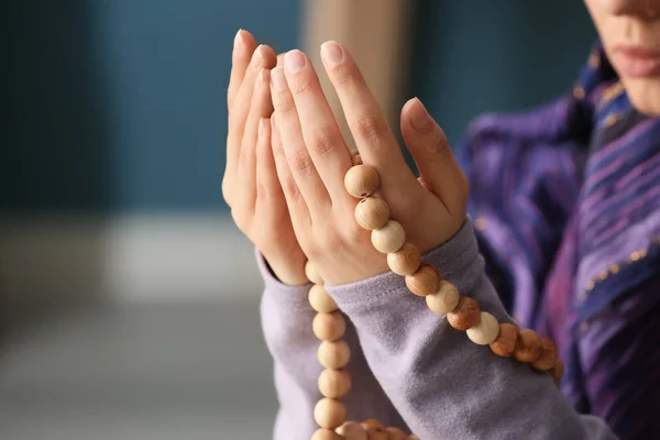 Young Muslim woman with rosary beads praying at home, closeup