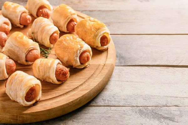 Fresh tasty sausage rolls on wooden board