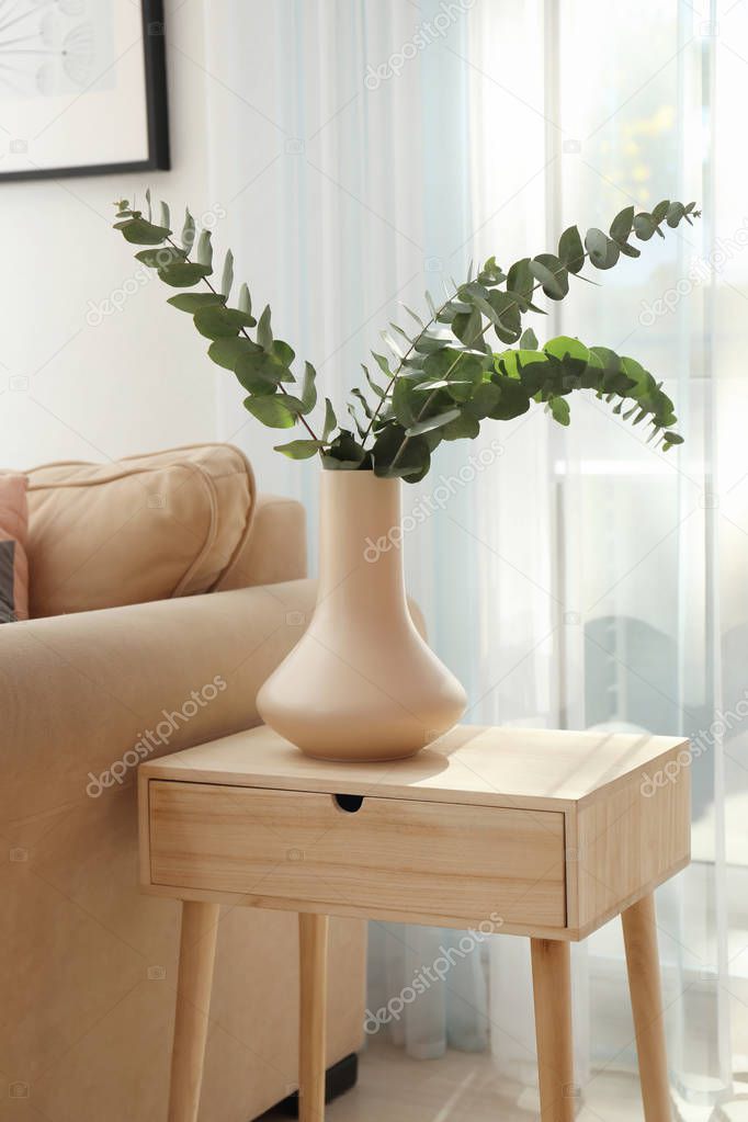 Vase with green eucalyptus branches on table in room