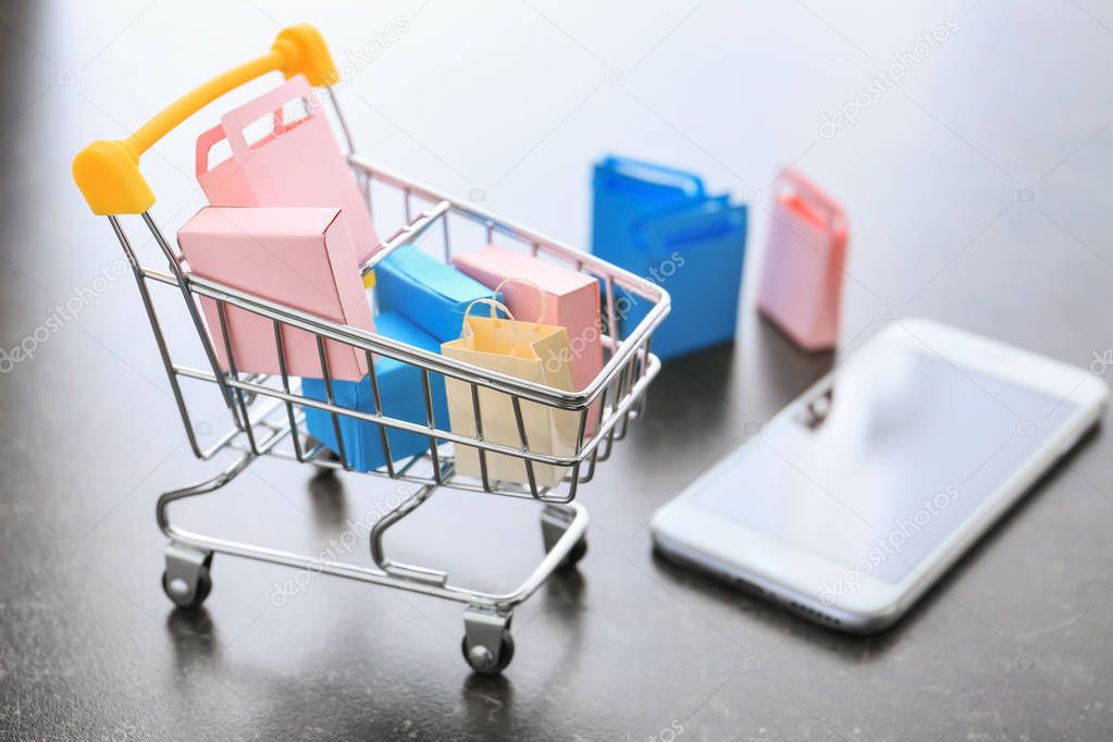 Small cart and mobile phone on table. Internet shopping concept