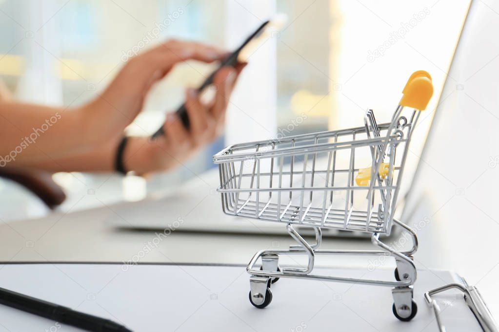 Small cart on table of woman using mobile phone and laptop. Internet shopping concept