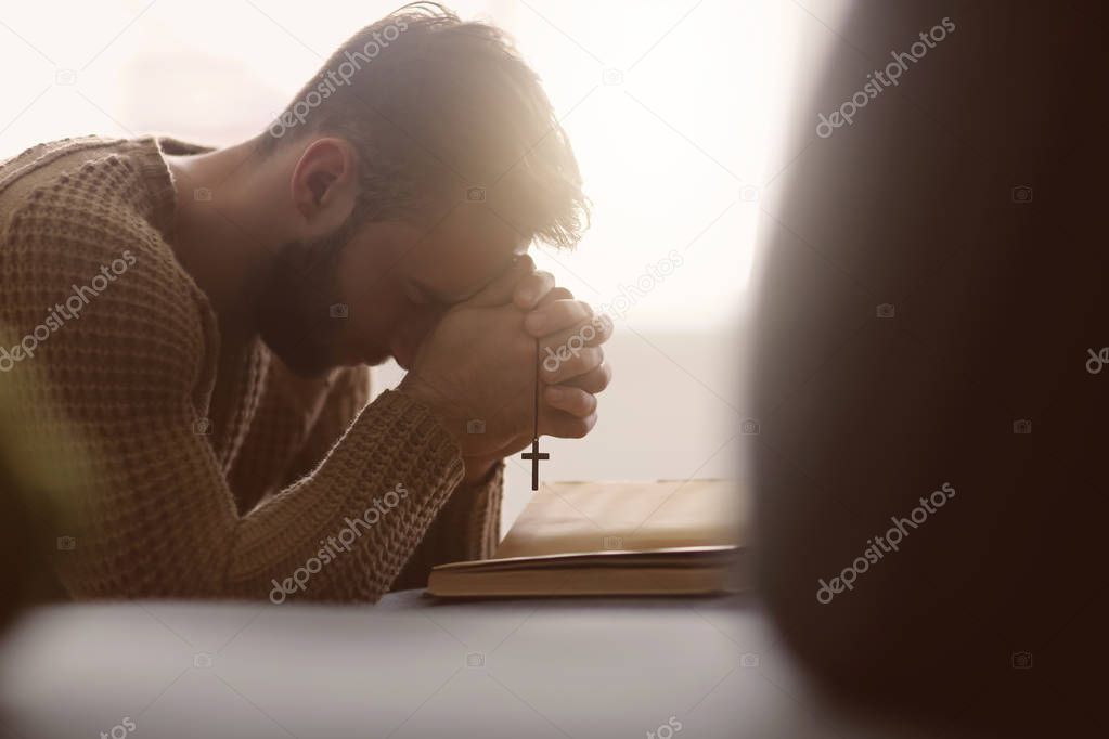 Religious young man praying to God at home