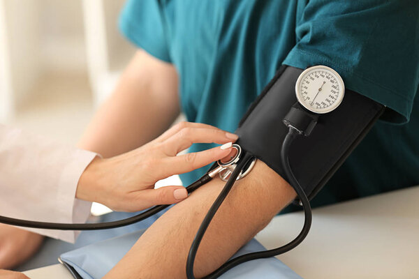 Female doctor measuring blood pressure of male patient in hospital