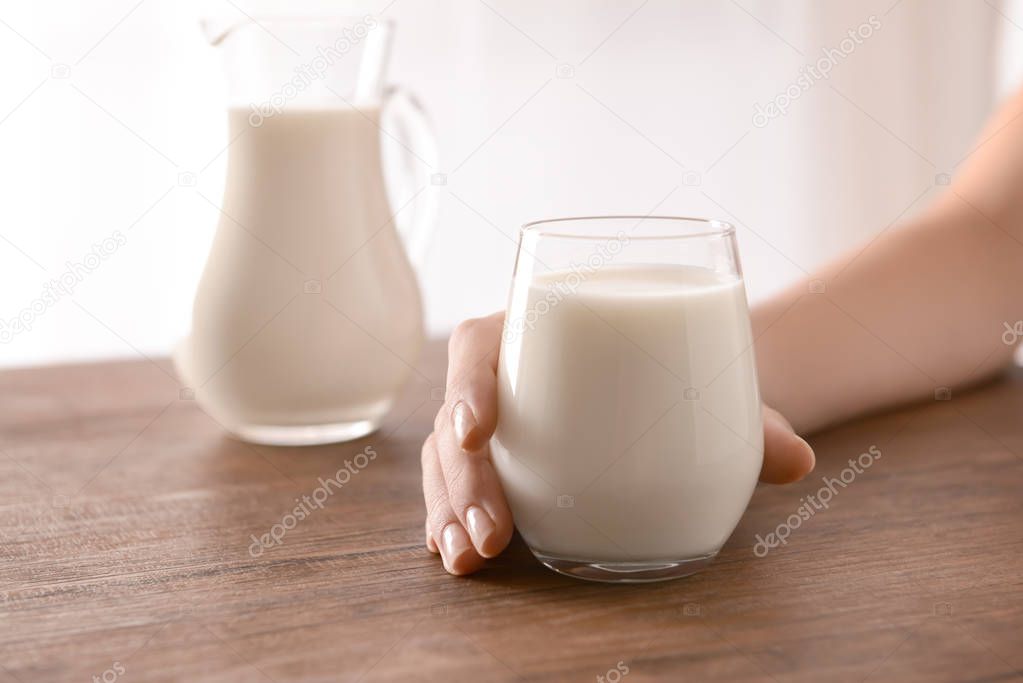 Female hand holding glass of tasty milk on wooden table