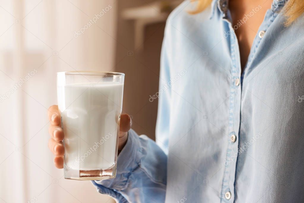 Woman holding glass of tasty milk indoors