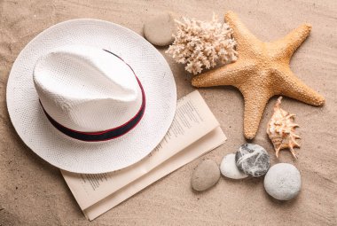 Deniz kabukları, deniz yıldızı ve gazete kum üstünde şapka