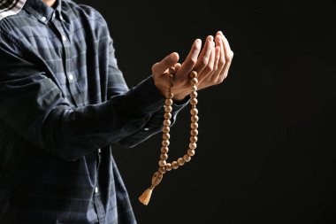 Genç Müslüman adam koyu arka plan üzerinde dua tespih ile