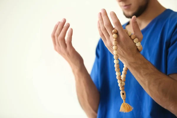Young Muslim man praying on light background