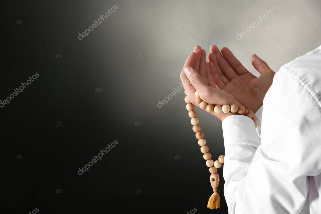 Young Muslim man with rosary beads praying on dark background, closeup