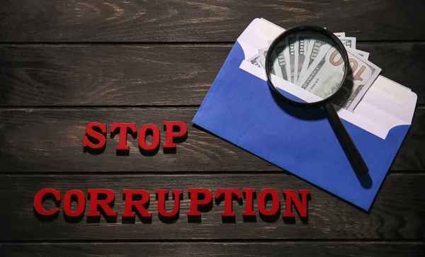 Text STOP CORRUPTION with money and magnifier glass on wooden background