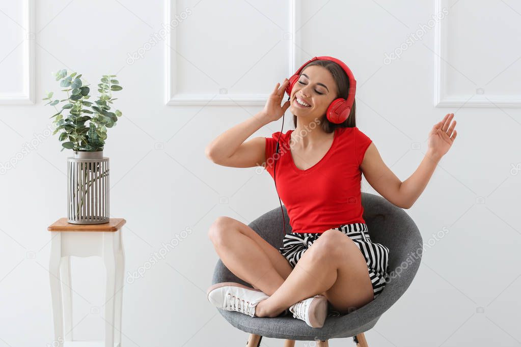 Beautiful woman listening to music while sitting in armchair near white wall