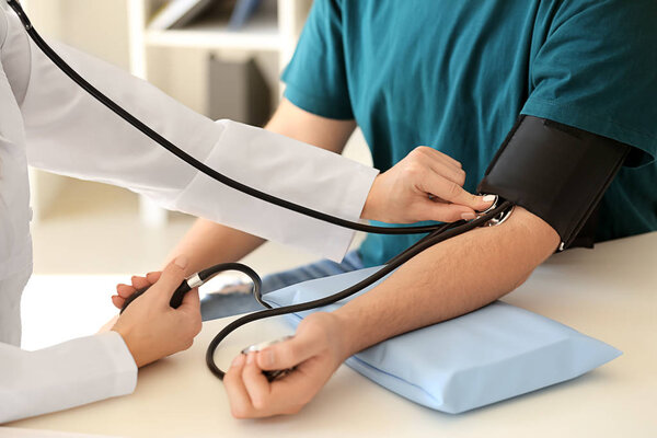Female doctor measuring blood pressure of male patient in hospital