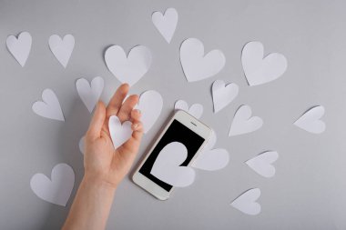 Kadın el Kağıt kalpleri ve gri arka plan, üstten görünüm üstünde hareket eden telefon