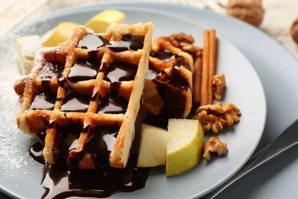 Tasty waffles with chocolate, fruit and walnuts on plate, closeup