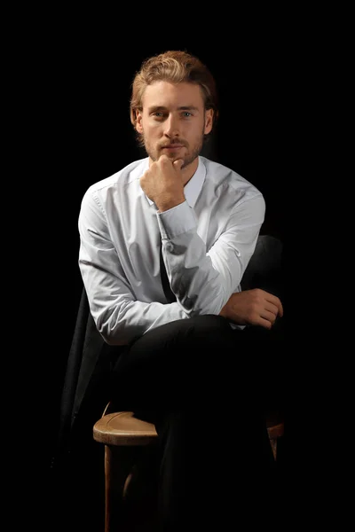 Handsome businessman sitting on chair against black background