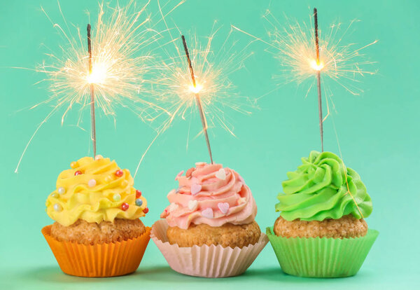 Tasty birthday cupcakes with sparklers on color background