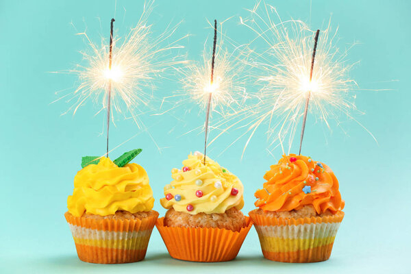 Tasty birthday cupcakes with sparklers on color background