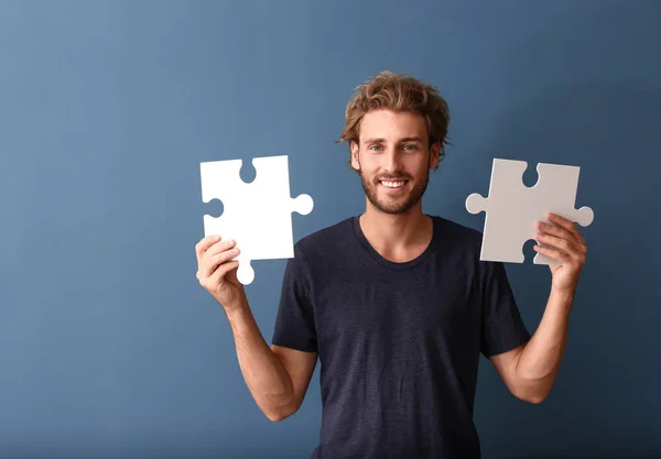 Young man with pieces of jigsaw puzzle on color background