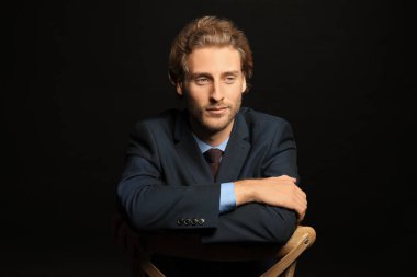 Siyah arka plan karşı sandalyeye oturan genç yakışıklı işadamı