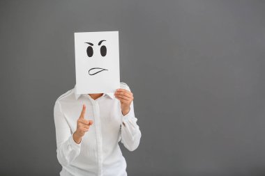 Genç kadın yüzü gri arka plan üzerinde çizilmiş ifade ile kağıdın arkasına saklanıyor