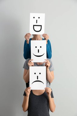 Genç kadın yüzleri yaprak kağıt üzerinde açık renkli çizilmiş emoticons ile arkasında saklanıyor