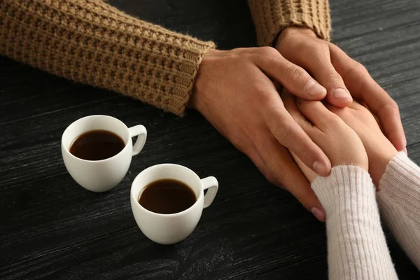 Loving young couple with cups of coffee on wooden background