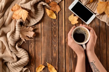 Fincan kahve, cep telefonu ve ahşap arka plan, üstten görünüm üzerinde sonbahar yaprakları ile eller