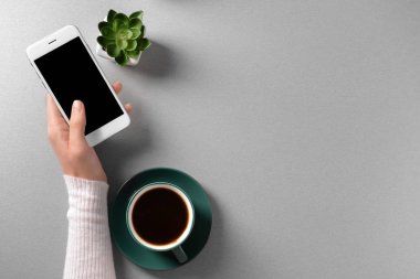 Kadın el cep telefonu ve fincan kahve açık renkli, üstten görünüm üzerinde